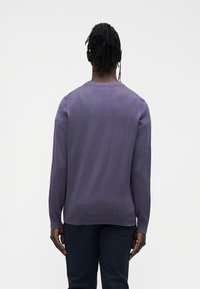 Maglione viola in maglia con maniche lunghe e collo rotondo. Tessuto liscio con sottili coste sull'orlo e sui polsini. Indossato sopra pantaloni scuri.