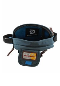 Marsupio in tessuto blu con apertura a zip, patch logo beige e giallo, fodera interna a fantasia e tracolla regolabile.