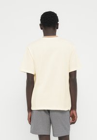 Κοντομάνικο ανοιχτό κίτρινο t-shirt, βαμβακερό υλικό, λαιμός σε στρογγυλή γραμμή, με διακριτική ριγωτή λεπτομέρεια στο γιακά, συνδυασμένο με σορτς καρό.