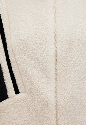 Cream fleece fabric with a soft, textured surface. Features a central seam and black striped accents along one side.