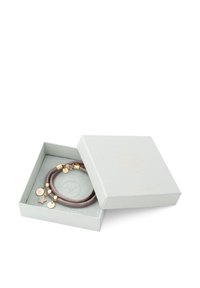 Bracelet en cuir marron avec des breloques dorées, incluant une étoile et des pendentifs circulaires, présenté dans une boîte cadeau grise avec un logo embossé.