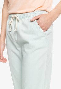 Pantalones de color verde menta claro, con cinta elástica en la cintura y cordón. Presentan bolsillos laterales y un corte holgado. Tejido de algodón suave y texturizado.