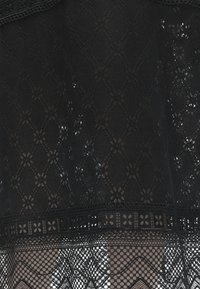 Μαύρο δαντελωτό ύφασμα με φυτικά και γεωμετρικά διαμαντένια σχέδια επάνω σε μπεζ φόντο, που εμφανίζει περίπλοκες διαφανείς λεπτομέρειες.