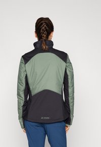 La veste présente un design noir et vert, avec un col haut et un tissu texturé sur les épaules et les manches, offrant un schéma de couleurs contrasté.