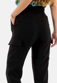 Pantalones cargo negros que cuentan con bolsillos laterales, un corte ajustado y una tela suave. La costura visible y un cinturón en la cintura realzan la funcionalidad del diseño.