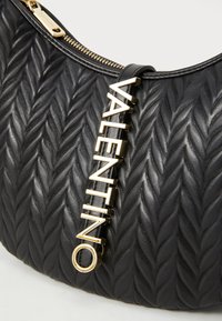 Borsa a tracolla in pelle nera con una trama tessuta testurizzata, dotata di un accento con logo dorato e di una chiusura lampo superiore.