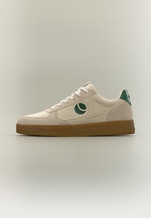 Beige lage sneaker met witte veters, groen logo aan de zijkant, groene hielstrook en een bruine rubberen zool.