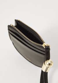 Black leather cardholder with a zipper, featuring gold hardware, multiple card slots, and a wrist strap. Textured surface and sleek design.
