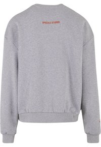Sweatshirt gris avec un col et un ourlet côtelés. Présente "UPSCALE STUDIOS" imprimé en rouge dans le haut du dos. Fabriqué en tissu doux et texturé.