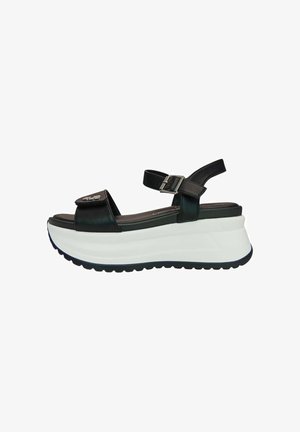 Sandalo platform in pelle nera con cinturino alla caviglia regolabile, suola bianca spessa e cinturino frontale in velcro con dettaglio logo metallico.