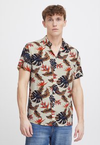 Camisa de botones de manga corta en beige con un patrón de hojas tropicales y flores en tonos azul marino, marrón y rojo. Tejido de mezcla de algodón.
