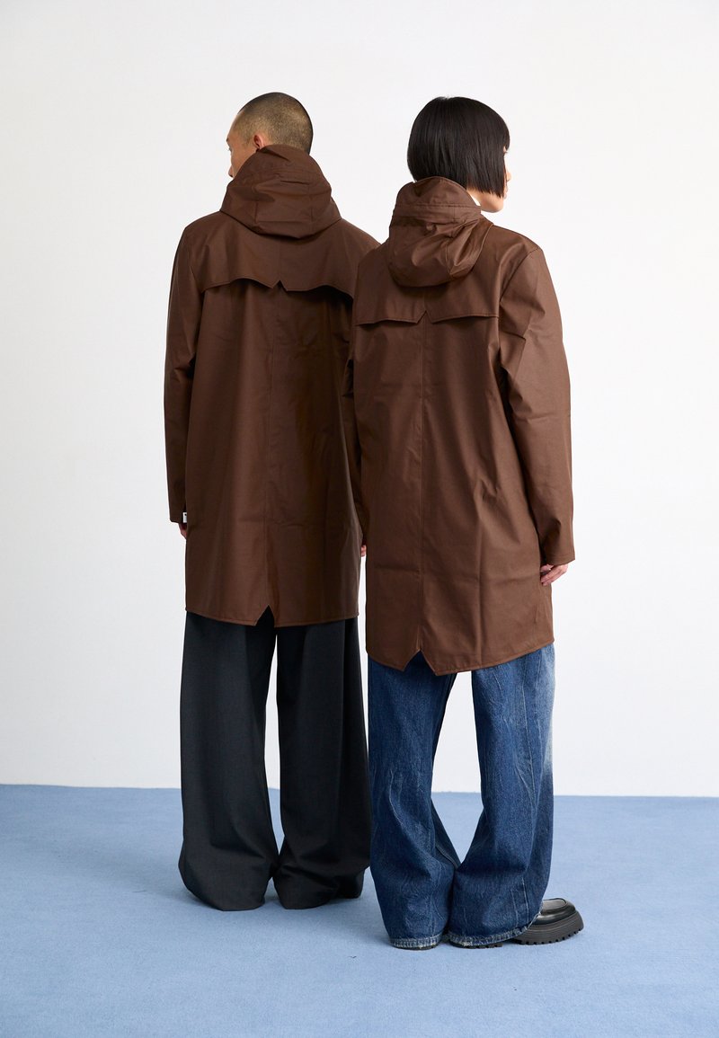 Brown waterproof jackets with hoods, featuring a layered design. One model wears dark gray pants, the other in light blue denim.