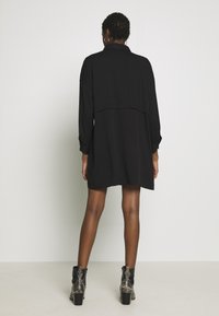 Abito nero con bottoni, maniche lunghe, vestibilità comoda, lunghezza a metà coscia e un design a strati sul retro. Indossato con stivali neri con tacco a stampa serpente.