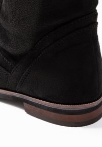 Stivale in suede nero con finitura testurizzata, dotato di suola in gomma marrone e dettagli di cucitura a contrasto lungo il bordo.