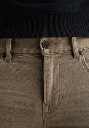 Primo piano di pantaloni kaki con bottone e cerniera, abbinati a un capo con cintura a coste nera.