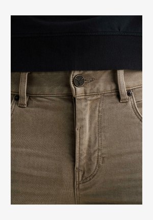 Primo piano di pantaloni kaki con bottone e cerniera, abbinati a un capo con cintura a coste nera.