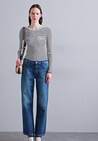 Long-sleeve striped shirt in black and white, paired with blue straight-leg jeans. A small shoulder bag features a branded strap.