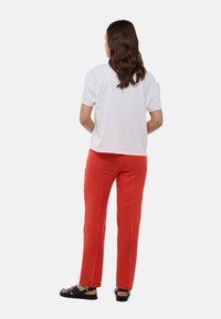T-shirt en coton blanc, coupe décontractée, associée à un pantalon en lin rouge vif. Sandales noires avec un détail de boucle. Vue de dos.