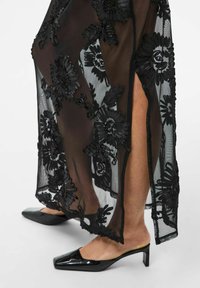 Mustast läbipaistvast kangast kleit lillemotiividega tikanditega, küljepealne lõhik, kombineeritud mustade teravate ninaosaga madala kandega kontsakingadega.