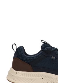 El zapato presenta una parte superior de malla azul marino, acentos de cuero marrón y una suela color crema moteada. Incluye una pestaña para tirar y cordones texturizados para un ajuste seguro.