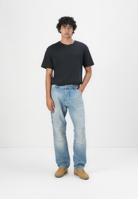Zwarte katoen t-shirt met een ronde hals, gecombineerd met lichtblauwe denim jeans met een relaxed fit en kniestukken. Lichtbruine schoenen.