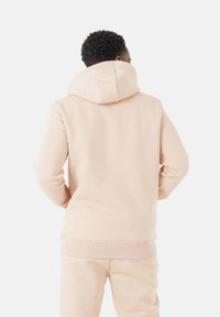 Sweatshirt à capuche rose clair en matériau doux, avec une coupe décontractée, des poignets côtelés et une capuche à double couche.