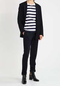 Czarna dopasowana marynarka, biało-granatowa koszulka w paski, granatowe spodnie i czarne botki na kostkę z blokowym obcasem. Czyste linie i dobrze zbudowany krój.