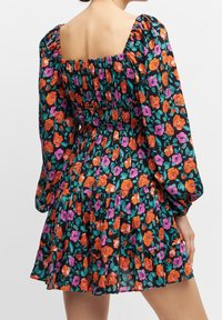 Robe fleurie avec un fond noir orné de roses orange et violettes, des manches bouffantes, un décolleté carré et un ourlet à volants.