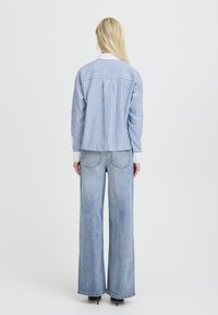 Blauw-wit gestreepte shirt met een kraag, gecombineerd met lichtblauwe wide-leg jeans met een hoge taille en rafelige randen.