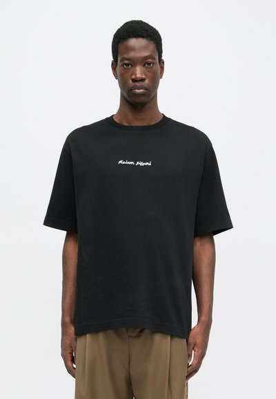 Schwarzes Baumwoll-T-Shirt mit Rundhalsausschnitt und kurzen Ärmeln. In der Mitte steht der weiß gestickte Text "Maison Kitsuné". Lockere Passform.