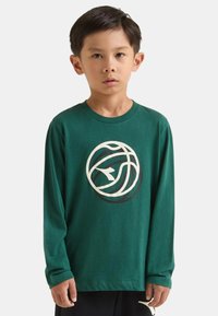 Maglietta verde a maniche lunghe in cotone, con un grande logo circolare bianco e nero sul davanti. Taglio casual con scollo a costine.