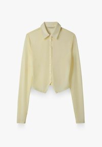 Chemise jaune clair à manches longues, boutonnée, avec col pointu et ourlet légèrement incurvé, présentée sur fond blanc.