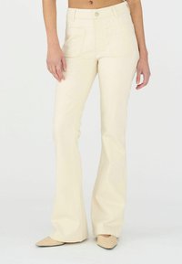 Pantalons évasés couleur crème avec une taille haute, comportant deux poches avant et une boutonnière, fabriqués en tissu lisse.