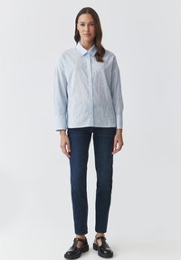 Camisa de botones azul claro con bordado floral, combinada con jeans azul oscuro y zapatos negros de tiras en T. Tejido suave y corte ajustado.