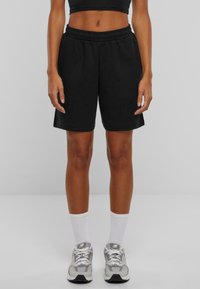 Shorts negri din bumbac cu talie elastică, până la genunchi, asociați cu șosete albe cu nervuri și pantofi sport gri deschis.