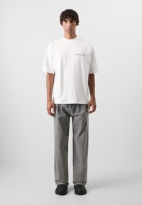 Hvid bomulds t-shirt med korte ærmer og trykt tekst "spild ikke kulturen", parret med løse grå bukser og sorte sneakers.