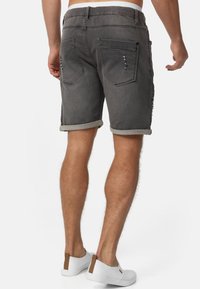 Graue Denim-Shorts mit hochgekrempeltem Saum, ausgestattet mit Gesäßtaschen und verwaschenen Details, kombiniert mit weißen Slippern.