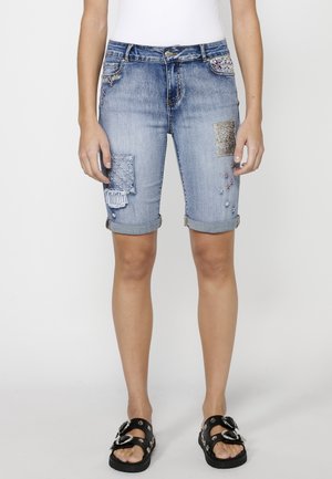 Shorts de mezclilla con tela azul clara, varios diseños de parches, dobladillos enrollados y acentos decorativos que incluyen cuentas y bordados.