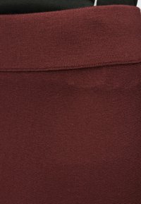 Material tricotat burgund cu textură nervurată, prevăzut cu o talie elastică neagră. Modelul este constant pe toată suprafața materialului.