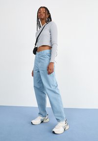 Pantaloni azzurri chiari, larghi e a vita alta con tasche laterali, abbinati a una maglietta grigia aderente a maniche lunghe e sneakers bianche.