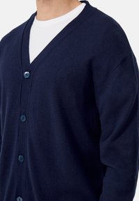 Námořnický modrý cardigan vyrobený z měkké tkaniny, s V-výstřihem, předními knoflíky a jemným logem na levém prsu.