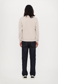 Beżowa bluza z okrągłym dekoltem i ściągaczami na rękawach, w połączeniu z ciemnoniebieskimi jeansami i białymi tenisówkami z czarnymi akcentami, widziana od tyłu.