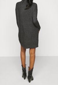 Abito in maglia grigio scuro con maniche lunghe e una vestibilità comoda, caratterizzato da un orlo che arriva sopra il ginocchio. Abbinato a stivali neri alla caviglia.
