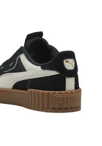 Zapatilla de ante en blanco y negro con una suela de goma texturizada, que presenta un acento en dorado del logo y un collar acolchado para mayor comodidad.