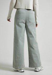 Kapeat, vaaleanvihreät farkut, joissa on leveät lahkeet ja takana kaksi taskua, joissa on sinisellä ommeltu aaltokuvio. Rentomallinen ja käännetyt lahkeet.