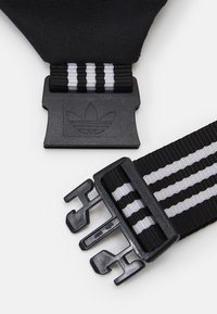 Black nylon belt featuring three white stripes, plastic buckle with embossed logo, and adjustable hardware for securing length.