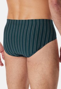 Slip da uomo in teal scuro con strisce verticali bianche. Presentano un'alta vita e un materiale elastico per comfort e vestibilità.