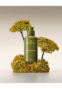 Bouteille vert foncé étiquetée "Plantscription" entourée de grappes de fleurs jaunes vives, sur un fond à dégradé doux.