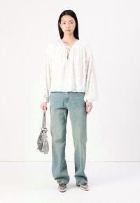 Weiße, strukturierte Bluse mit langen Puffärmeln und einem Schlüssellochausschnitt, kombiniert mit hellblauen geraden Jeans und einer silbernen Handtasche.
