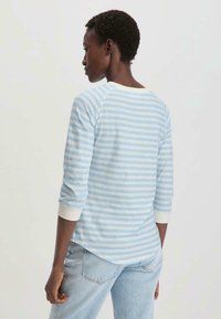 Vaaleansini-valkoinen raitapaita pitkällä hihalla, jossa on pyöreä kaula-aukko ja raglan-hihat. Paidassa on ribattu hihansuu ja kaareva helma.